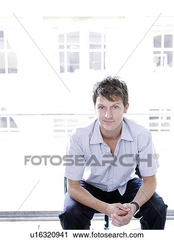 Stock Image - Man sitting, hands together, at window. Fotosearch