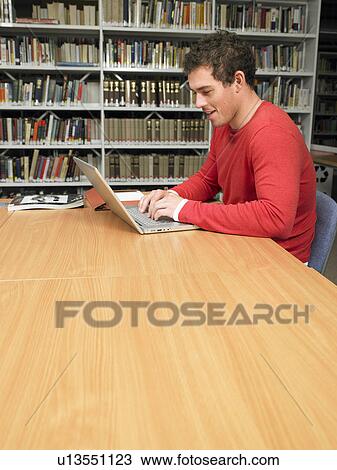 Young man working at computer in library View Large Photo Image Stock Image - Young man working at computer in library. Fotosearch