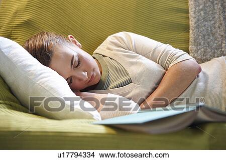 Picture - Young woman lying on couch, with book. Fotosearch