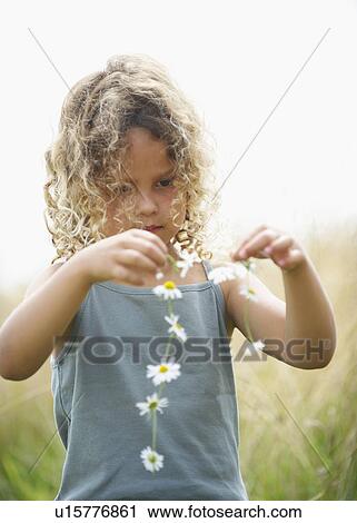 Stock Image - Young girl making a daisy chain. Fotosearch