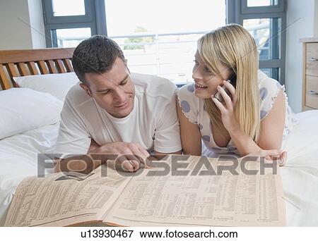 Stock Photo - Couple check stocks and shares in bed. Fotosearch