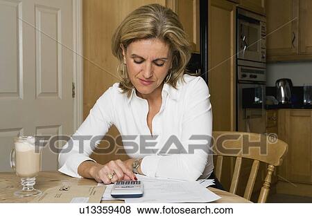 Woman using calculator at kitchen table View Large Photo Image Stock Photo - Woman using calculator at kitchen table. Fotosearch