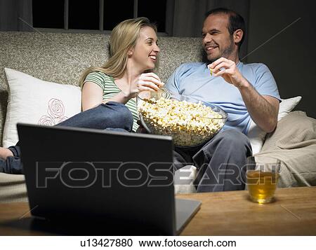 Young couple sharing popcorn on couch View Large Photo Image Stock Image - Young couple sharing popcorn on couch. Fotosearch
