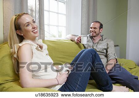 Couple sitting on couch, with mugs View Large Photo Image Stock Image - Couple sitting on couch, with mugs. Fotosearch