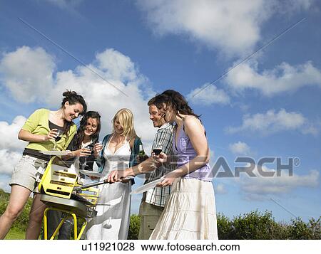 Stock Photo - Group of young people around barbecue. Fotosearch
