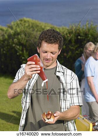 Man pouring ketchup onto hot dog View Large Photo Image Stock Image - Man pouring ketchup onto hot dog. Fotosearch