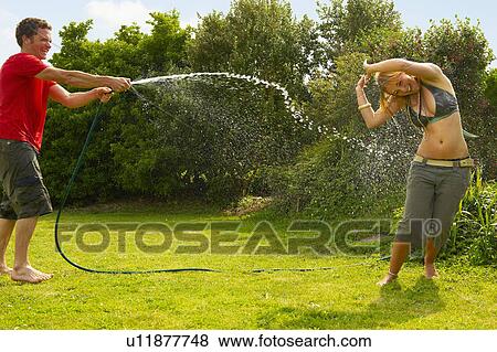 Stock Photo - Man spraying woman with garden hose. Fotosearch