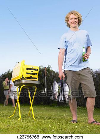 Young man holding fish next to barbecue View Large Photo Image Stock Photo - Young man holding fish next to barbecue. Fotosearch