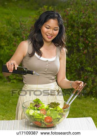 Stock Photo - Young woman pouring olive oil on salad. Fotosearch