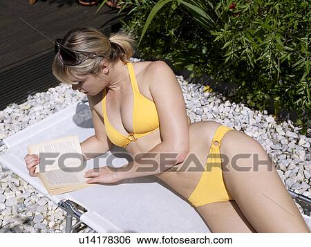 Stock Photograph - Young woman in bikini in garden reading. Fotosearch