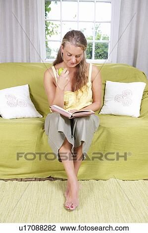 Stock Image - Young woman reading on couch. Fotosearch