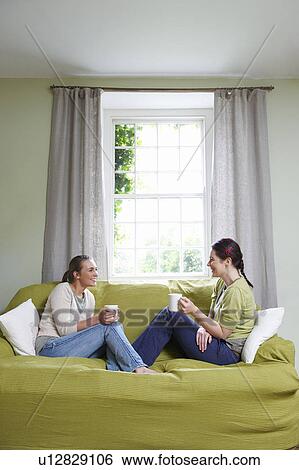 Two young women on couch, with mugs View Large Photo Image Stock Photograph - Two young women on couch, with mugs. Fotosearch