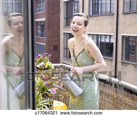 Stock Image - Woman on balcony watering flowers. Fotosearch
