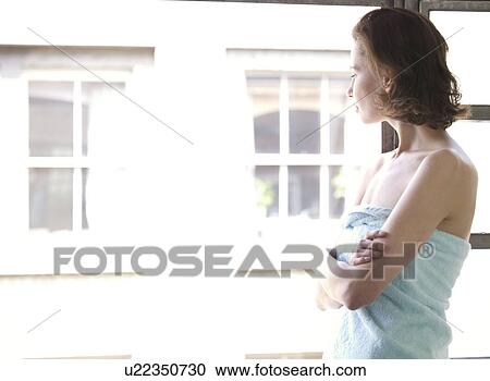 Stock Image - Woman standing looking out of window. Fotosearch