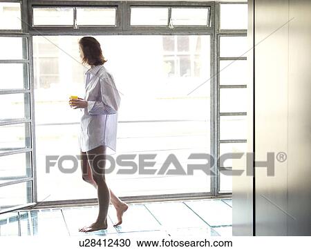 Stock Image - Woman walking past window in morning. Fotosearch