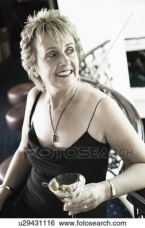 Close-up of a mature woman holding a glass of cocktail and smiling View Large Photo Image Stock Photograph - Close-up of a mature woman holding a glass of cocktail and smiling. Fotosearch