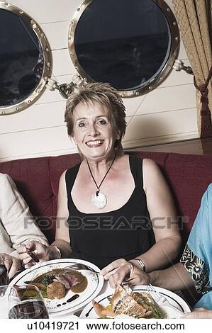 Portrait of a mature woman sitting at a table and taking food View Large Photo Image Stock Image - Portrait of a mature woman sitting at a table and taking food. Fotosearch