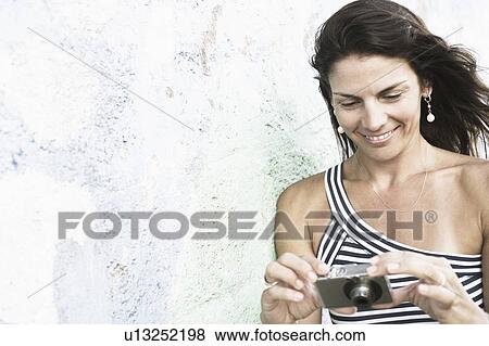 Close-up of a mid adult woman holding a digital camera and smiling View Large Photo Image Stock Photo - Close-up of a mid adult woman holding a digital camera and smiling. Fotosearch