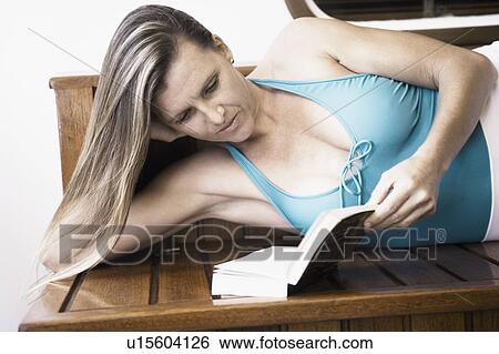Close-up of a mid adult woman lying on a bench and reading a book View Large Photo Image Stock Photograph - Close-up of a mid adult woman lying on a bench and reading a book. Fotosearch