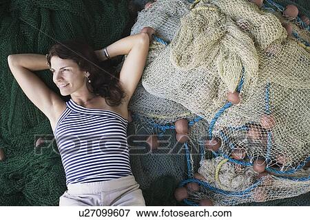 Stock Photo - High angle view of a mid adult woman lying on commercial fishing nets and smiling. Fotosearch
