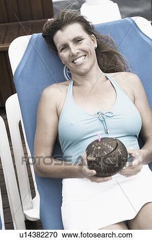 Mid adult woman reclining on a lounge chair and smiling View Large Photo Image Stock Image - Mid adult woman reclining on a lounge chair and smiling. Fotosearch