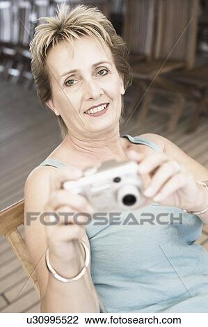 Portrait of a mature woman holding a digital camera and smiling View Large Photo Image Stock Image - Portrait of a mature woman holding a digital camera and smiling. Fotosearch