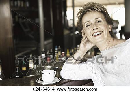 Portrait of a mature woman leaning against a bar counter and smiling View Large Photo Image Picture - Portrait of a mature woman leaning against a bar counter and smiling. Fotosearch