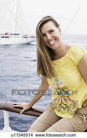 Portrait of a mid adult woman sitting on a railing and smiling View Large Photo Image Picture - Portrait of a mid adult woman sitting on a railing and smiling. Fotosearch