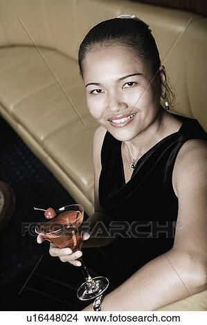 Portrait of a young woman holding a glass of martini and smiling View Large Photo Image Picture - Portrait of a young woman holding a glass of martini and smiling. Fotosearch