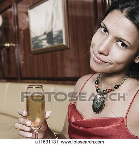 Portrait of a young woman holding a champagne flute and smiling View Large Photo Image Stock Image - Portrait of a young woman holding a champagne flute and smiling. Fotosearch