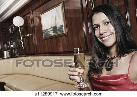 Portrait of a young woman holding a champagne flute and smiling View Large Photo Image Stock Photo - Portrait of a young woman holding a champagne flute and smiling. Fotosearch