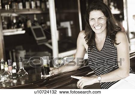 Stock Image - Close-up of a mid adult woman sitting at a bar counter and holding a glass of whiskey. Fotosearch