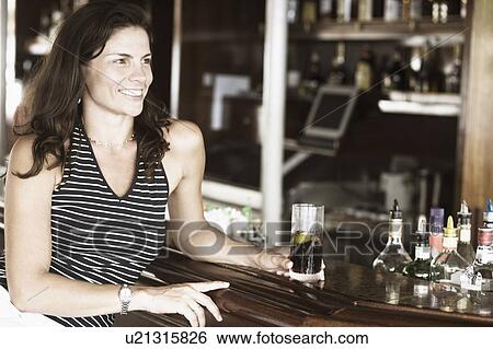 Close-up of a mid adult woman sitting at a bar counter and holding a glass of whiskey View Large Photo Image Stock Photograph - Close-up of a mid adult woman sitting at a bar counter and holding a glass of whiskey. Fotosearch