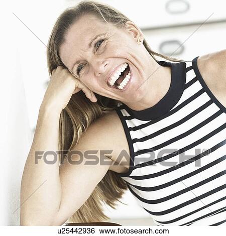 Stock Photograph - Mid adult woman laughing with her head in her hand. Fotosearch
