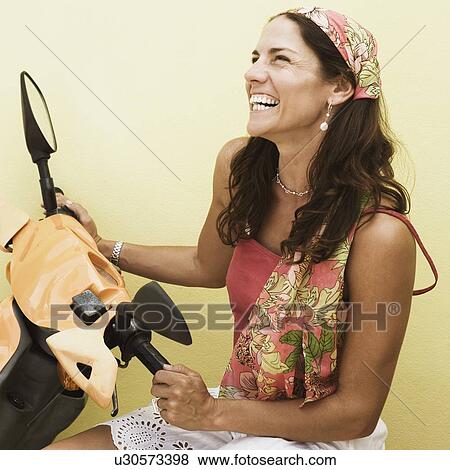 Mid adult woman sitting on a motor scooter and smiling View Large Photo Image Stock Photo - Mid adult woman sitting on a motor scooter and smiling. Fotosearch
