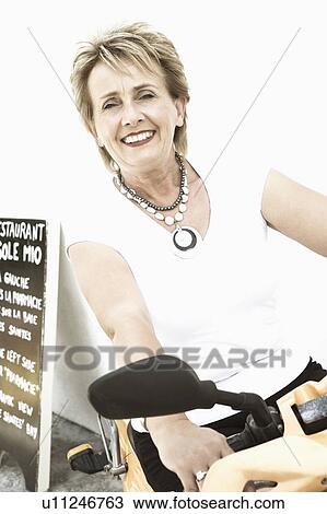 Portrait of a mature woman sitting on a motor scooter and smiling View Large Photo Image Stock Image - Portrait of a mature woman sitting on a motor scooter and smiling. Fotosearch
