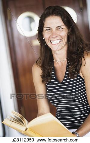Stock Image - Portrait of a mid adult woman holding a book and smiling. Fotosearch