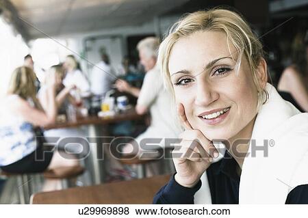 Portrait of a young woman smiling with her hand on her chin in a restaurant View Large Photo Image Stock Photo - Portrait of a young woman smiling with her hand on her chin in a restaurant. Fotosearch