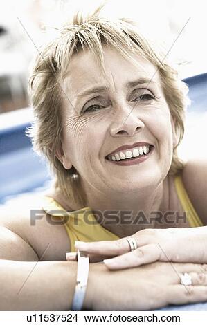 Close-up of a mature woman leaning on the ledge of a swimming pool and smiling View Large Photo Image Picture - Close-up of a mature woman leaning on the ledge of a swimming pool and smiling. Fotosearch