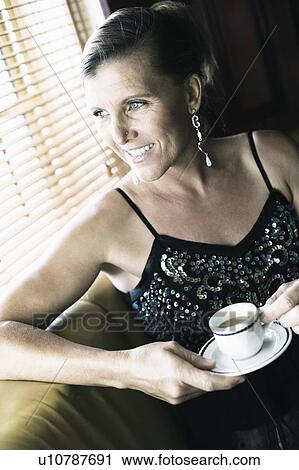 Stock Image - Close-up of a mid adult woman holding a cup of tea with a saucer and smiling. Fotosearch
