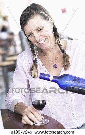 Stock Photography - Close-up of a mid adult woman pouring wine into a wine glass and smiling. Fotosearch