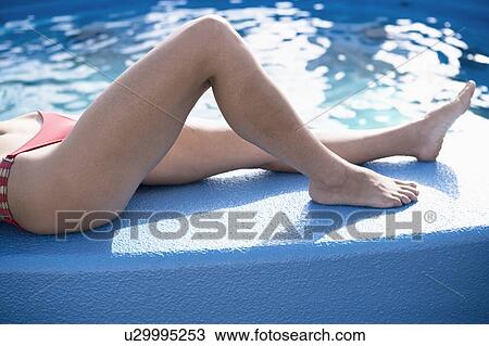 Stock Image - Low section view of a woman lying on the ledge of a swimming pool. Fotosearch