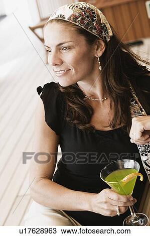 Stock Image - Mid adult woman holding a glass of cocktail and smiling. Fotosearch