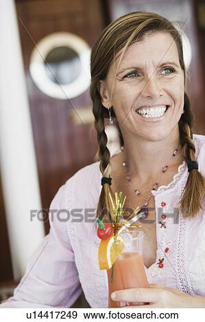 Mid adult woman holding a glass of cocktail and smiling View Large Photo Image Stock Photo - Mid adult woman holding a glass of cocktail and smiling. Fotosearch