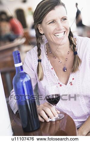 Stock Photograph - Mid adult woman sitting at a table and holding a glass of wine. Fotosearch