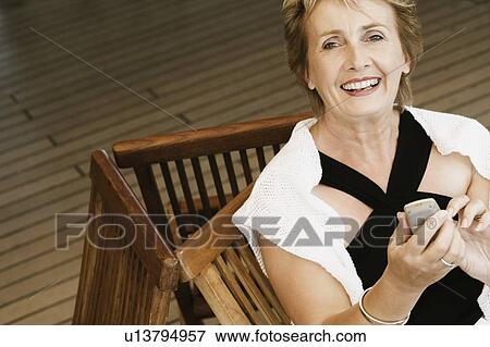 Portrait of a mature woman sitting on a chair and holding a mobile phone View Large Photo Image Stock Photo - Portrait of a mature woman sitting on a chair and holding a mobile phone. Fotosearch