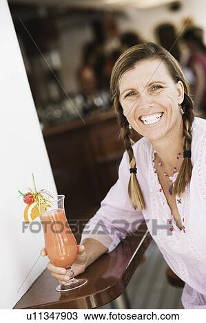 Portrait of a mid adult woman holding a glass of cocktail and smiling View Large Photo Image Stock Image - Portrait of a mid adult woman holding a glass of cocktail and smiling. Fotosearch