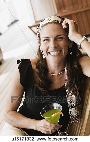 Portrait of a mid adult woman holding a glass of cocktail and smiling View Large Photo Image Stock Image - Portrait of a mid adult woman holding a glass of cocktail and smiling. Fotosearch