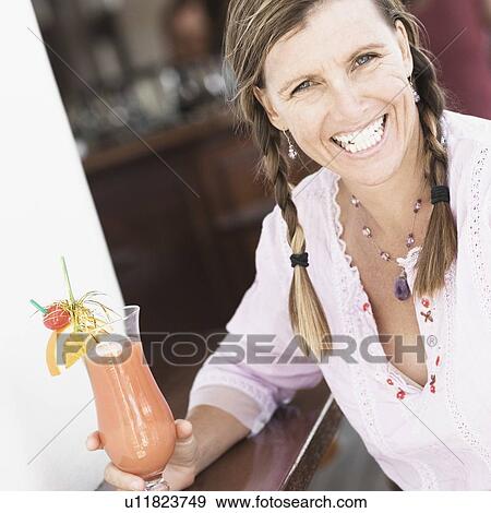 Portrait of a mid adult woman holding a glass of cocktail and smiling View Large Photo Image Stock Photo - Portrait of a mid adult woman holding a glass of cocktail and smiling. Fotosearch