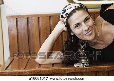 Portrait of a mid adult woman lying on a bench and smiling View Large Photo Image Stock Photo - Portrait of a mid adult woman lying on a bench and smiling. Fotosearch